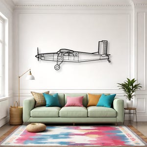 May include: Black metal airplane wall art. The airplane has a propeller, a cockpit, and a tail. The wall art is mounted on a white wall above a green sofa with colorful pillows and a patterned rug.