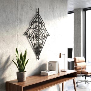May include: A black metal wall art piece featuring a diamond-shaped geometric frame with intricate internal lines, concentric circles, and a fan-like pattern at the bottom, mounted on a textured gray concrete wall above a wooden console table.