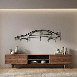 Könnte beinhalten: Schwarze Metall-Wandkunst mit Umrissen eines Autos. Das Kunstwerk ist an einer hellgrauen Wand über einer Holz-TV-Konsole angebracht. Die Konsole hat zwei Türen, ein offenes Regal, eine kleine Pflanze und Bücher.