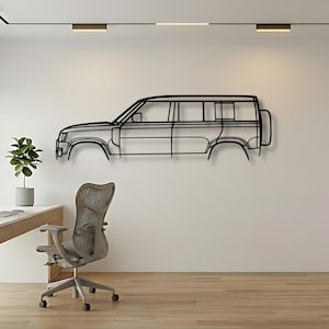 Puede incluir: Arte mural de metal negro que representa el contorno de un vehículo, montado en una pared blanca. La obra de arte es un perfil lateral de un coche, con detalles de las ventanas, puertas y ruedas. Un escritorio, una silla y una planta están en primer plano.