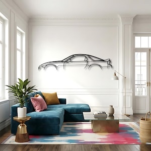 Könnte beinhalten: Schwarze Metall-Wandkunst, die das Seitenprofil eines Sportwagens zeigt. Das Kunstwerk ist an einer weißen Wand über einem tealfarbenen Ecksofa angebracht. Der Raum verfügt außerdem über einen bunten Teppich, einen goldenen Beistelltisch und eine Stehlampe.