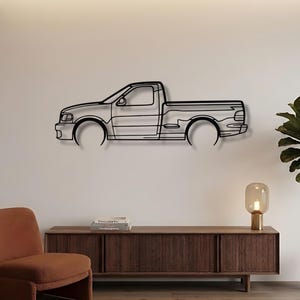 May include: A black metal wall art piece depicting a pickup truck silhouette. The artwork is mounted on a white wall, showcasing the vehicle's side profile. The design includes the cab, bed, and wheel wells.