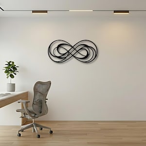 May include: A black metal wall art piece featuring an intricate, continuous infinity loop design with multiple overlapping curves and swirling lines, mounted horizontally on a plain white wall above a desk and office chair setup.