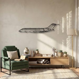 Op de afbeelding: Zwarte metalen vliegtuig wandkunst. Het kunstwerk is een zijaanzicht van een straalvliegtuig, gemonteerd op een neutraal gekleurde muur. De kamer heeft ook een groene fauteuil, houten meubels en een vloerlamp.