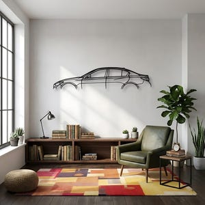 May include: A black metal car outline wall art decor. The artwork is mounted on a white wall above a wooden bookshelf. The room features a green armchair, a colorful rug, and a potted plant.