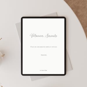 May include: A black tablet displaying the text "Planner Serenite" in elegant script. Below, smaller text reads "POUR UNE ORGANISATION SIMPLE & EFFICACE" and "Essentiel". The tablet rests on a light gray surface, suggesting a planner or organizational tool.