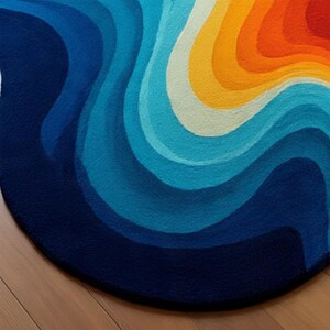 May include: A round rug with a layered design in shades of blue, transitioning to yellow and orange. The rug's pattern resembles a topographical map or abstract waves, creating a visually dynamic and colorful accent for any room.