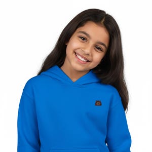 May include: A bright blue hoodie with a small embroidered patch on the chest. The patch features a brown bear design. The hoodie has a hood and long sleeves. The person wearing the hoodie is smiling.