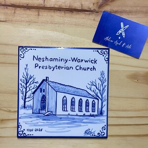 Op de afbeelding: Een vierkante keramische tegel met een blauw-witte handgeschilderde illustratie van de Neshaminy-Warwick Presbyterian Church. De tekst luidt Neshaminy-Warwick Presbyterian Church en 1726-2026. Een blauw visitekaartje met de tekst Atelier Azul & Arte.
