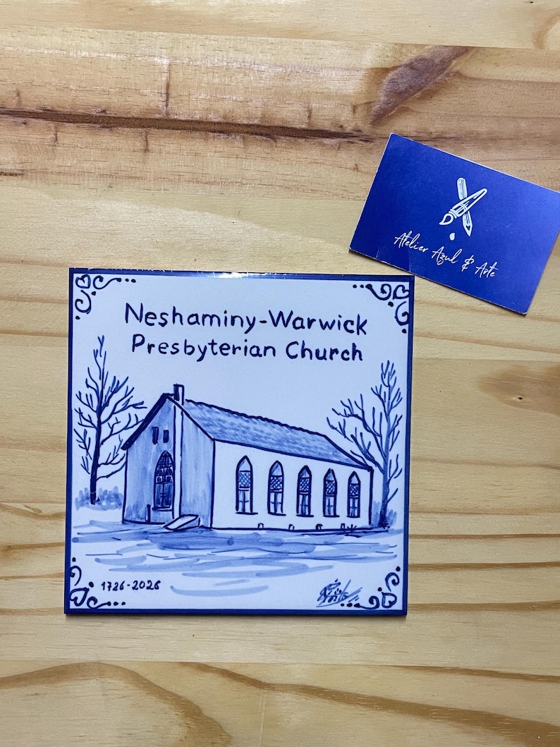Op de afbeelding: Een vierkante keramische tegel met een blauw-witte handgeschilderde illustratie van de Neshaminy-Warwick Presbyterian Church. De tekst luidt Neshaminy-Warwick Presbyterian Church en 1726-2026. Een blauw visitekaartje met de tekst Atelier Azul & Arte.