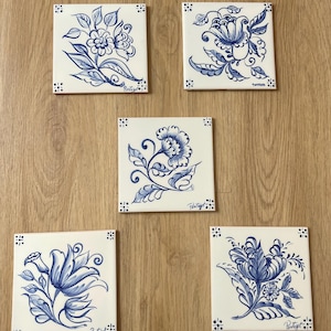 Pode incluir: Cinco azulejos de cerâmica quadrados com desenhos florais azuis pintados à mão sobre um fundo branco. Cada azulejo apresenta uma ilustração botânica única com folhas e pétalas em espiral, com a palavra Portugal escrita no canto.