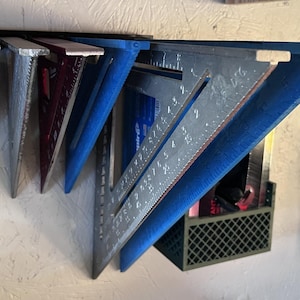 May include: A wall-mounted tool organiser with several metal speed squares in various colours. The organiser is blue and black, and a small green crate holds extra tools. A pair of scissors hangs nearby.