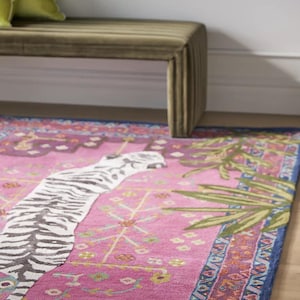 May include: A vibrant pink rug with a zebra stripe design and botanical accents. The rug features a blue border and a decorative pattern. A green bench and pillows are in the background.