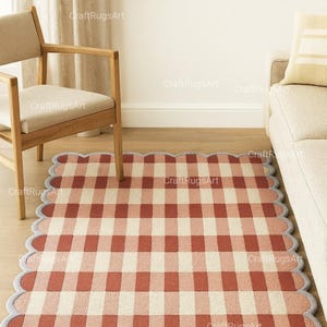Może przedstawiać: Czerwono-kremowy dywan w kratę z falistą krawędzią. Dywan jest prostokątny i położony na drewnianej podłodze. W tle drewniane krzesło i sofa. Wymiary dywanu nie są widoczne.