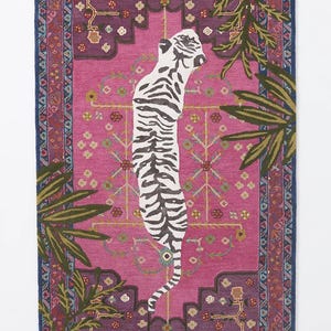 May include: A rectangular rug with a pink center featuring a white and black tiger design. The rug has a dark blue border with a repeating pattern and green and brown palm fronds on the sides. The rug measures approximately 60 inches long and 40 inches wide.