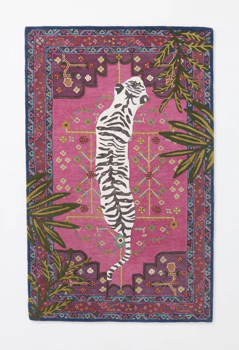 May include: A rectangular rug with a pink center featuring a white and black tiger design. The rug has a dark blue border with a repeating pattern and green and brown palm fronds on the sides. The rug measures approximately 60 inches long and 40 inches wide.