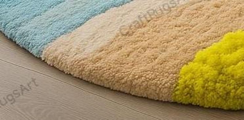 Pode incluir: Um close-up de um tapete redondo e colorido com uma superf&iacute;cie texturizada. O tapete apresenta sec&ccedil;&otilde;es azuis, bege e amarelas. O tapete est&aacute; colocado sobre um ch&atilde;o de madeira clara.