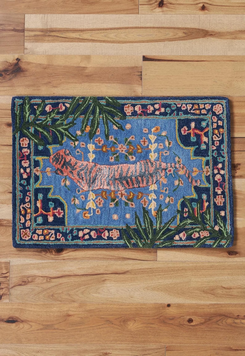 May include: Rectangular rug with a blue background and a tiger design. The tiger is orange with black stripes. The rug has a dark blue border with floral and leaf accents. The rug is placed on a wooden floor.