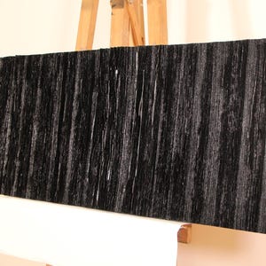 Peut inclure: Une œuvre d'art rectangulaire en bois noir avec des rainures verticales. L'œuvre est présentée sur un chevalet en bois, mettant en valeur sa surface texturée et sa couleur sombre. Esthétique moderne et minimaliste.