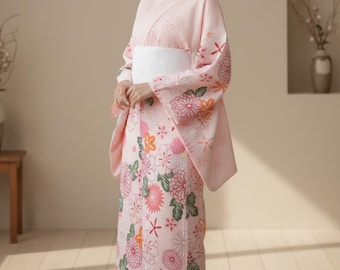 May include: A light pink kimono with a floral pattern featuring pink, orange, and green flowers. The kimono has long sleeves and a white obi belt. The fabric appears soft and flowing, suitable for traditional Japanese attire.