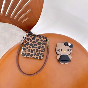 May include: A small, leopard print bag with a brown strap and silver-colored hardware. A cartoon figure of a cat with a black dress and bow is also present.