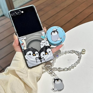 May include: A phone case, pop socket, and charm with a penguin theme. The phone case has a black and white cartoon penguin design. The pop socket is light blue with a penguin design. A pearl bracelet with a penguin charm is also included.