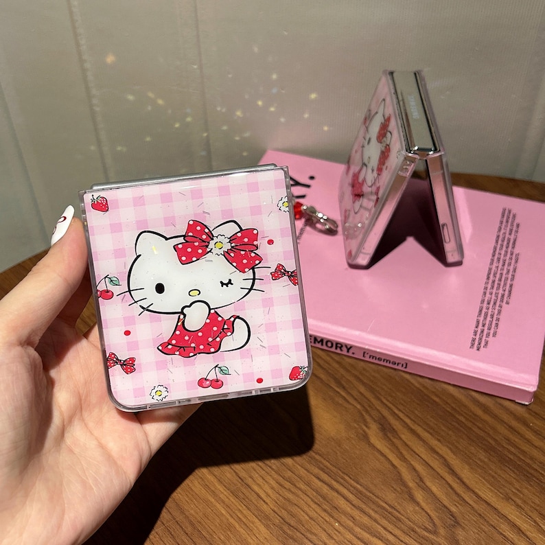 May include: Pink phone case featuring a Hello Kitty design with a red bow and dress, set against a pink gingham pattern. The case is shown open and closed, with a matching design on the back.