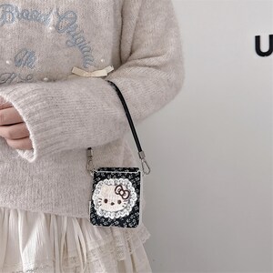 May include: A black floral print case with a Hello Kitty design, featuring a white face, a red bow, and a white lace border. The case has a black strap and silver-tone metal clasps.