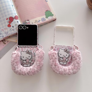 Op de afbeelding: Twee roze en witte Hello Kitty telefoonhoesjes met een pluizige, harige band. De hoesjes hebben een roze luipaardprint en een cartoonafbeelding van Hello Kitty. De telefoonschermen zijn zwart.