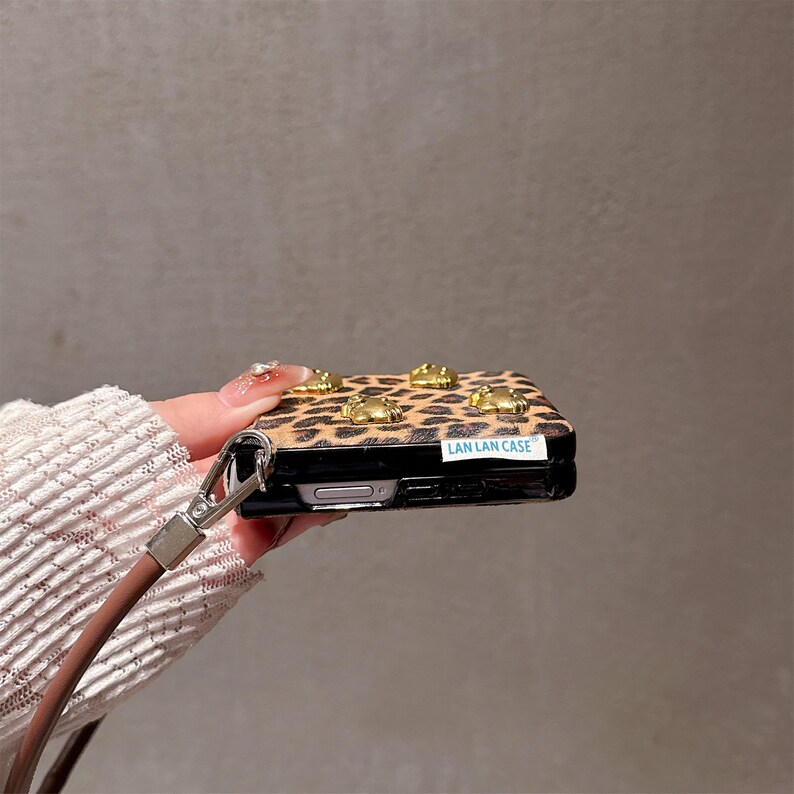 May include: A leopard print phone case with gold-colored embellishments. The case has a brown strap and the text "LAN LAN CASE".