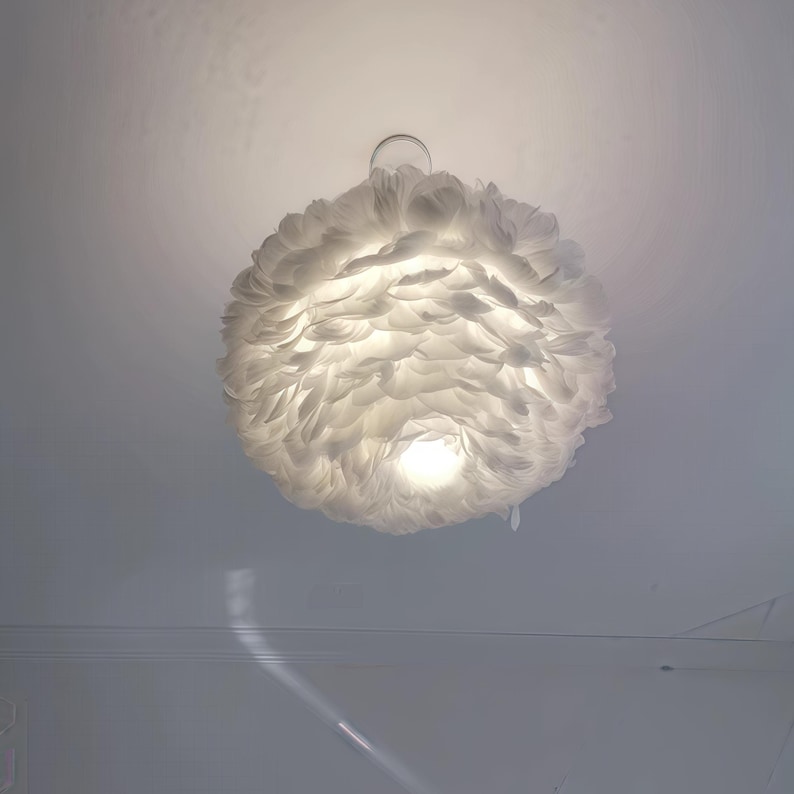 May include: A white, feathery pendant light fitting. The light is spherical and appears to be made of many individual feathers. The light is on, and the bulb is visible in the centre.