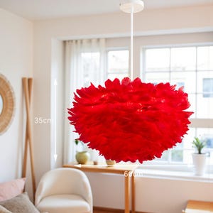 May include: A striking red feather pendant light, 60cm wide and 35cm tall, suspended from a white ceiling fitting. The light fixture is the centrepiece of a bright room, with a window and a white chair visible.