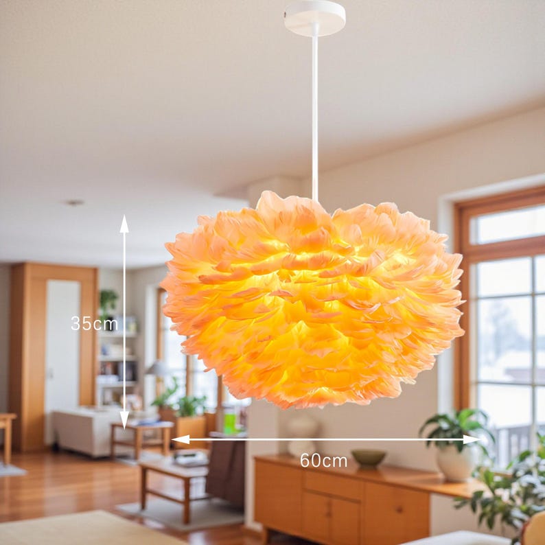 May include: A pendant light with a lampshade resembling feathers, in orange and yellow hues. The lampshade is 60cm wide and 35cm tall. The light hangs from a white ceiling fixture, suitable for interior lighting.