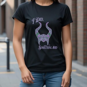 May include: Black t-shirt featuring the text "I Did. Something Bad" in a stylized font. The shirt design includes a purple and green horned silhouette. The shirt is paired with blue jeans.