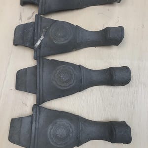 May include: Four dark gray cast iron furniture legs. Each leg has a decorative floral medallion and a curved, tapered design. The legs are arranged on a light wood surface.