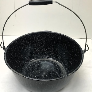 May include: A black speckled enamelware pot with a metal handle and wire bail. The pot is round with a wide opening and a black handle. The interior is black with white speckles.