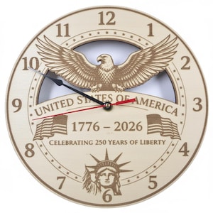May include: A round wooden clock with a light brown finish. The clock face features an eagle with outstretched wings, the text "UNITED STATES OF AMERICA", and the years "1776-2026". The clock hands are black and red.
