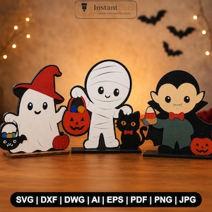 May include: Three wooden Halloween tabletop decorations featuring a white ghost in a red hat holding a pumpkin bucket, a white mummy with a black cat, and a vampire in a black cape holding candy corn, all standing on individual rectangular bases.