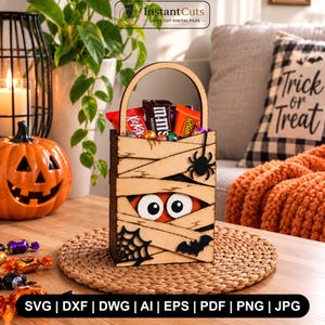 Könnte beinhalten: Ein hölzerner Halloween-Süßigkeitenkorb im Mumien-Design mit geschichteten Bandagen, großen weißen Augen, einer schwarzen Spinne und einer Fledermaus-Aussparung. Der rechteckige Behälter hat einen geschwungenen Griff und ist mit Süßigkeiten gefüllt.