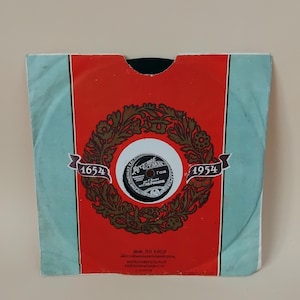 Pode incluir: Disco de vinil vintage em uma capa vermelha e azul. A capa apresenta um design floral central com os anos 1654 e 1954 em faixas. O rótulo do disco é visível, com texto em um layout circular.