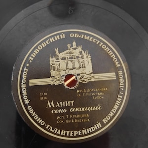 Pode incluir: Um disco de vinil vintage com um rótulo castanho escuro com texto cirílico e uma ilustração dourada de um edifício. O rótulo inclui o texto "МАНИТ сень акаций" e outros detalhes.