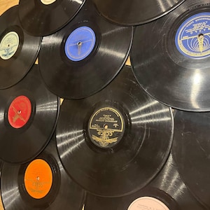Pode incluir: Uma coleção de discos de vinil vintage com discos pretos e rótulos coloridos. Os rótulos apresentam várias cores, incluindo azul, vermelho, laranja e amarelo. Os discos estão dispostos em um padrão de close-up sobreposto.