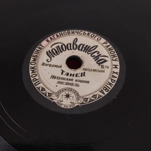 Pode incluir: Close-up de um disco de vinil preto com um rótulo branco e preto. O rótulo apresenta texto cirílico, incluindo a palavra "Moldavaneska" e a palavra "Dança". Um item de música vintage.