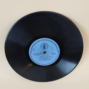 Pode incluir: Um disco de vinil preto vintage com um rótulo azul claro. O rótulo apresenta texto cirílico e um logotipo. O disco é um disco de 7 polegadas, um formato clássico para música. Um item de colecionador de música vintage.