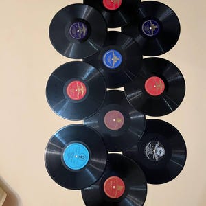 Pode incluir: Uma coleção de dez discos de vinil pretos com rótulos coloridos, incluindo vermelho, azul e roxo. Os discos estão dispostos verticalmente, mostrando uma variedade de álbuns de música vintage.
