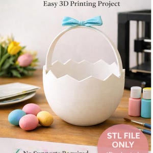 May include: A white 3D-printed Easter egg basket with a blue bow on the handle. The egg-shaped basket has a jagged top edge and is displayed with colorful Easter eggs and paint supplies. Text on the image reads "Print, Fill, Decorate".