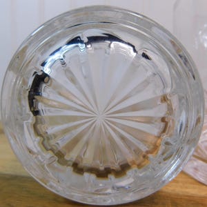 Pode incluir: Close-up da base de um copo transparente com um padr&atilde;o circular em forma de leque. O copo tem uma base espessa e est&aacute; parcialmente desfocado. O copo est&aacute; sobre uma superf&iacute;cie de madeira.