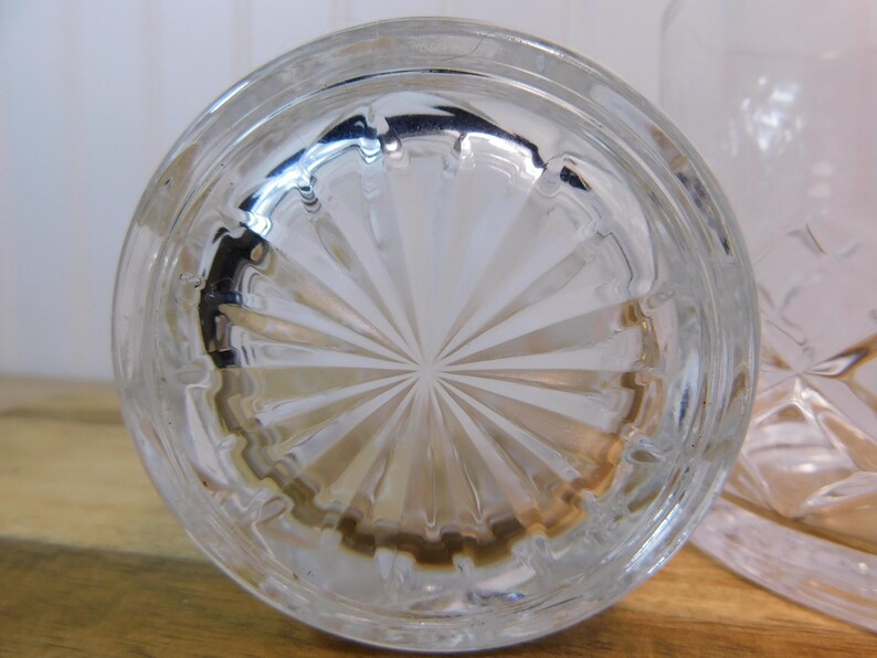 Pode incluir: Close-up da base de um copo transparente com um padr&atilde;o circular em forma de leque. O copo tem uma base espessa e est&aacute; parcialmente desfocado. O copo est&aacute; sobre uma superf&iacute;cie de madeira.