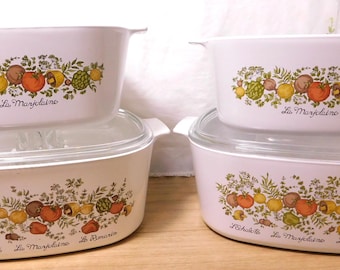May include: Set of four white casserole dishes with glass lids. Each dish features a colorful floral and vegetable design with the words "La Marjolaine" and other French text. The dishes are ideal for baking and serving.