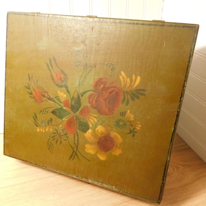 May include: A vintage wooden box with a painted floral design. The flowers are in shades of red, yellow, and orange, with green leaves and stems. The box has a distressed, olive green background and is likely used for storage.